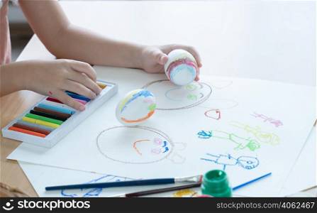 Selective focus on Easter egg in hand of little kid girl while choosing crayon color to decorate egg. Cute child prepare for Easter holiday at home. Children education by drawing and painting