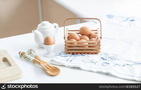 Selective focus on fresh egg placed on egg stand in home kitchen with raw chicken eggs in basket, wooden spoon and fork and cutting board placed on table. Eggs for ingredient in breakfast concept