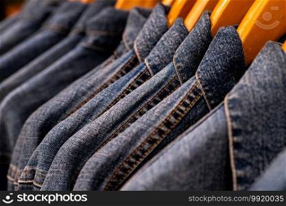 Selective focus on jacket jeans hanging on rack in clothes shop. Denim jeans with jeans pattern. Textile industry. Jeans fashion and shopping concept. Clothing concept. Denim jacket on rack for sale.