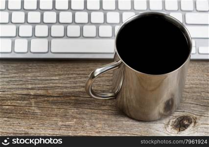 Selective focus on lip of coffee mug with partial keyboard in background. Layout in horizontal format on rustic wood.