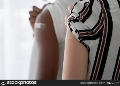 Selective focus on medicated plaster stuck on upper arm of Caucasian young woman rolling up sleeves to show that she get vaccinated. Dark skinned man on blur background