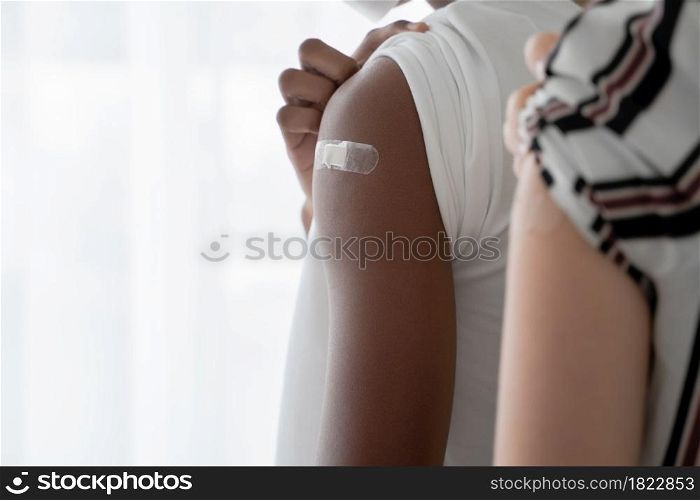 Selective focus on medicated plaster stuck on upper arm of dark skinned young man wear mask rolling up sleeves to show that he get vaccinated. Caucasian woman on blur foreground. White background