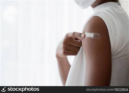 Selective focus on medicated plaster stuck on upper arm of dark skinned man wear mask pointing at plaster. White background. Concept for people to get vaccinated to prevent corona virus