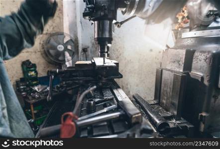 Selective focus on milling machine. Blurred worker is working on milling machine to milling metal plate. Tool for cut metal workpiece. Steel manufacturing factory. Milling process. Machine in workshop