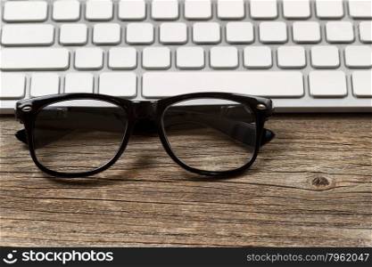 Selective focus on reading glasses with partial keyboard in background. Layout in horizontal format on rustic wood.