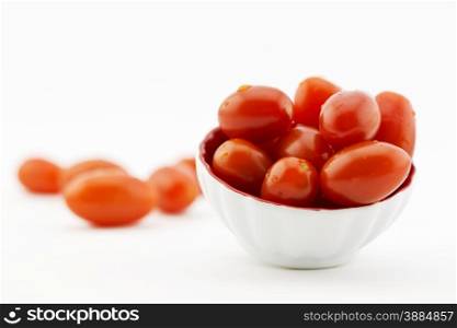 Selective focus on red cherry tomatoes in small white dish with crimson interior; copy space available on horizontal image. Shallow depth of field results in loose cherry tomatoes in background being out of focus. Damp droplets on produce.