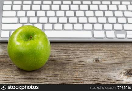 Selective focus on ripe green apple with partial keyboard in background. Layout in horizontal format on rustic wood.