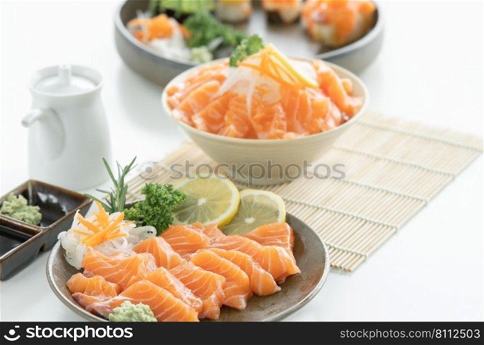 Selective focus on sliced salmon sashimi in plate served with wasabi, soy sauce, sliced lemon and radish at kitchen. Salmon on ice and sushi on blur background. Japanese food home cooked concept