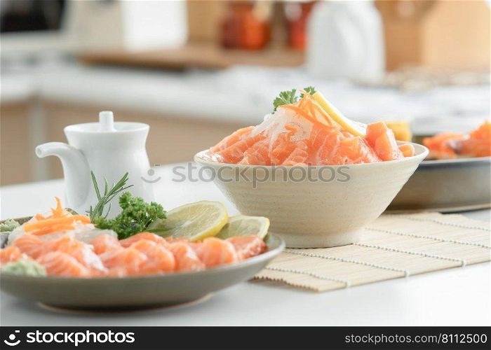 Selective focus on sliced salmon sashimi on ice in white bowl served with wasabi, soy sauce in small jug, sliced lemon and radish at kitchen. Japanese food home cooked concept