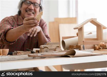 Selective focus on small wooden Christmas tree model in Asian white haired senior carpenter man?s hand. He smiling and showing wood work he made with pride at workplace at home. White background