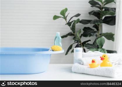 Selective focus on sponge and liquid soap or sh&oo bottle are place on blue bathtub. Two yellow ducks toys on towel, talc powder, body lotion are near tub on table. Baby shower accessories concept