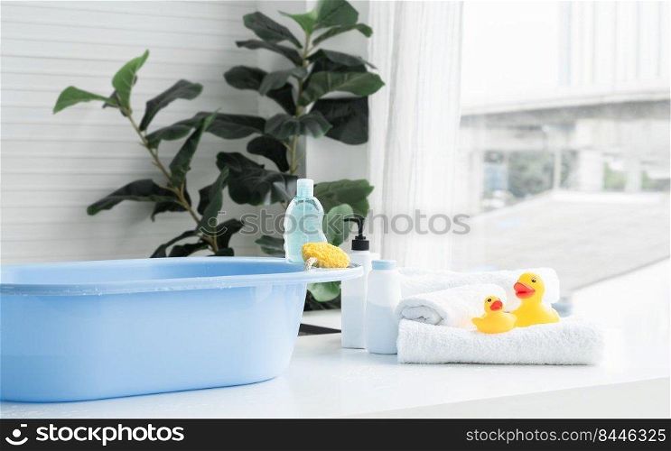 Selective focus on sponge and liquid soap or shampoo bottle are place on blue bathtub. Two yellow ducks toys on towel, talc powder, body lotion are near tub on table. Baby shower accessories concept