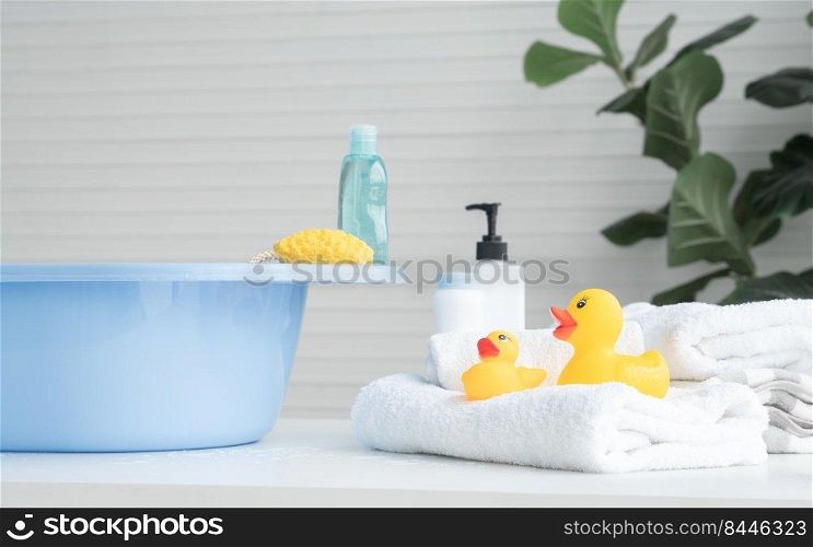 Selective focus on two yellow ducks toys on towel. Sponge and liquid soap or shampoo bottle are place on blue bathtub, talc powder, body lotion are near tub on table. Baby shower accessories concept