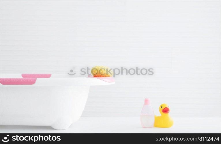 Selective focus on yellow sponge on white and pink baby bathtub near pink sh&oo or shower gel bottle and yellow rubber duck toy in bathroom. White background. Copy space