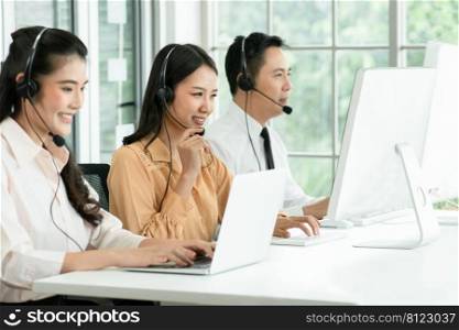 Selective focus on young operator woman touching microphone on headset and working with smiling and doing customer support at work. Group of Asian employee work in telemarketing customer service teams
