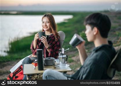 Selective focus,  Pretty girl smiling,  Asian young couple sitting drinking coffee to happily near lake and front of tent on c&ing trip. Lifestyle and c&ing concept.