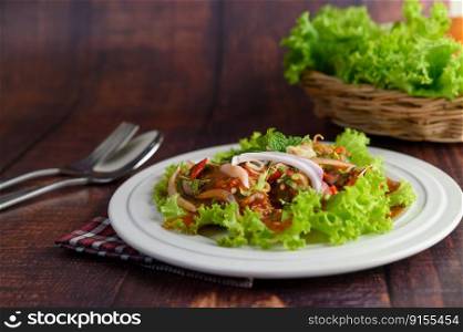 Selective focus Spicy salad of sardine with tomato sauce mixed with herb in white dish and sparken stainless spoon and fork over napkin on wooden table, copy space