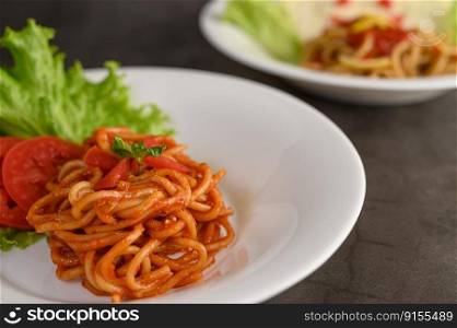 Selective focus the Stir fried spaghetti with tomato sauce and tomato slice with lettuce in white plate, copy space