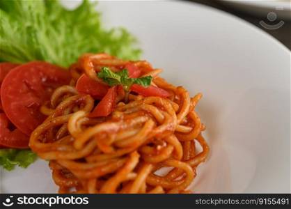 Selective focus the Stir fried spaghetti with tomato sauce and tomato slice with lettuce in white plate, copy space
