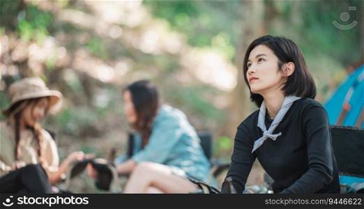 Selective focus, Young Asian pretty woman and her girlfriend sitting at front of tent, use mobile phone take photo during camping in forest with happiness together