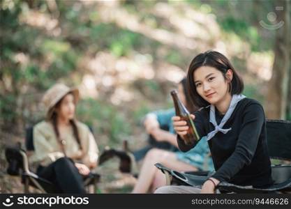Selective focus young Asian pretty woman and her girlfriend sitting at front of tent, use mobile phone take photo during camping in forest with happiness together