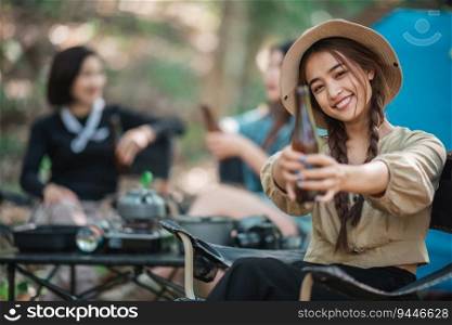 Selective focus young Asian pretty woman and her girlfriend sitting at front of tent, use mobile phone take photo during c&ing in forest with happiness together