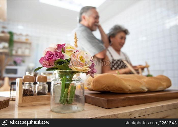 Selective focused on rose on table in kitchen with elder senior asian couple cooking dinner in background.love is all around and everywhere.