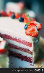 Selective macro focus vertical image of delicious cake with white icing decorated with fresh strawberries, blueberries, on white plate. Image for menu or confectionery catalog