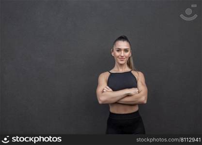 Self assured female athlete in sportswear crossing arms and looking at camera while taking break in fitness training against black wall in gym. Confident sportswoman with crossed arms