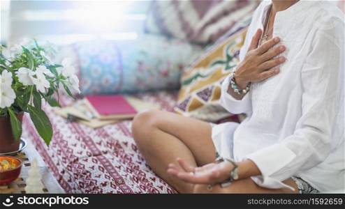 Self-Healing Heart Chakra Meditation. Woman sitting in a lotus position with right hand on heart chakra and left palm open in a receiving gesture. Self-Care Practice at Home. Mindfulness and Open Heart Meditation, Spiritual Awakening