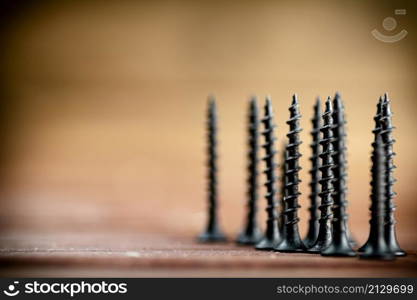 Self-tapping screw on wood on the table. On a wooden background. High quality photo. Self-tapping screw on wood on the table.