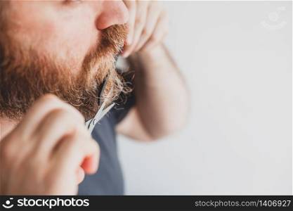 Selfcare during quarantine isolation. Adult handsome caucasian man cutting moustache and beard himself personally with scissors at home. Coronavirus outbreak and people shutdown, stay home concept