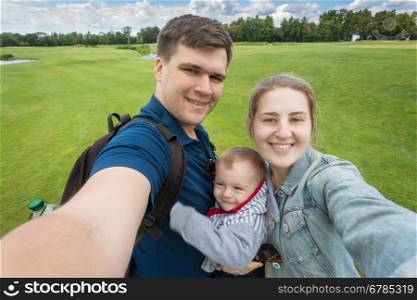 Selfie image of happy family with cute baby boy relaxing at park