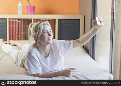 Selfie in bed! Full length of beautiful young woman using her smart phone with smile while lying down on her bed