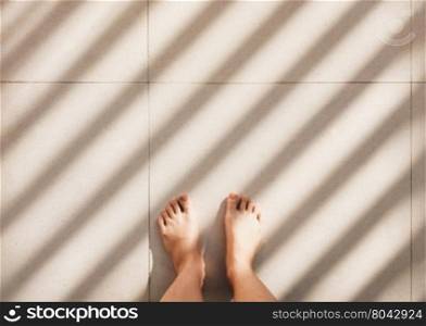 Selfie of barefoot standing on pavement floor background with light and shadow, top view