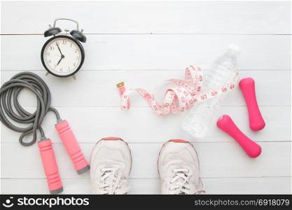 Selfie of feet sport shoes and fitness items measuring-tape and alarm clock on white wooden floor, Healthy lifestyle