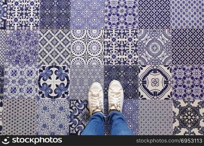 Selfie of feet with sneaker shoes on art pattern tiles floor background, top view