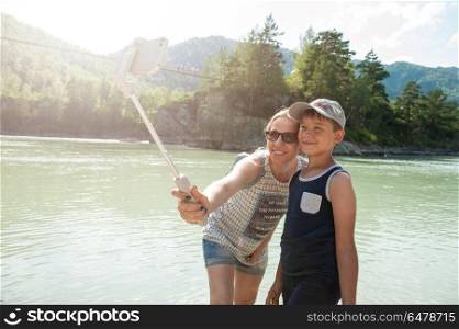 selfie on mobile phone with stick. Mother and son taking selfie on mobile phone with stick. Vacation on river in the mountain