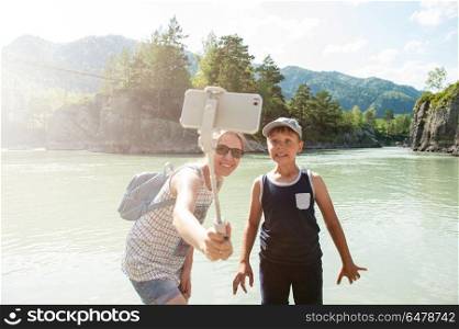selfie on mobile phone with stick. Mother and son taking selfie on mobile phone with stick. Vacation on river in the mountain