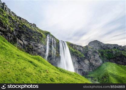 Seljalandsfoss waterfalls in Iceland with green hills and lava cliffs