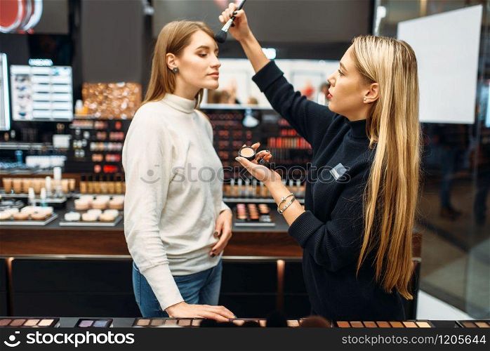 Seller consultant and woman testing powder in the make-up shop. Cosmetic choosing in beauty store
