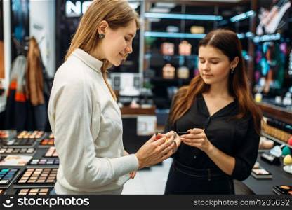 Seller consultant helps the woman with the choice of shadows shade in the make-up shop. Cosmetic choosing in beauty store
