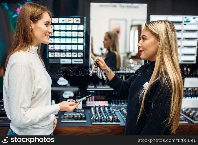 Seller consultant shows to female client eyeshadows in the make-up shop. Cosmetics choosing in beauty store, makeup store. Seller shows to client eyeshadows in make-up shop