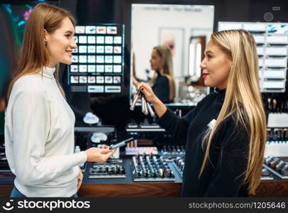 Seller consultant shows to female client eyeshadows in the make-up shop. Cosmetics choosing in beauty store, makeup store. Seller shows to client eyeshadows in make-up shop