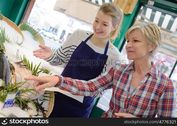 seller helping woman purchasing fish in supermarket