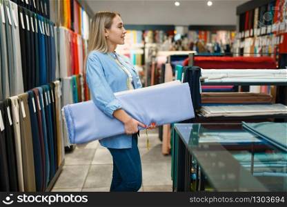 Seller holds stack of fabric in textile store. Shelf with cloth for sewing on background, clothing patterns choice in shop. Seller holds stack of fabric in textile store