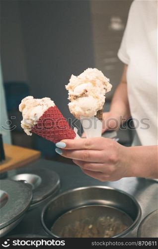 Seller selling couple scoops of ice cream in a candy shop by a street. Woman putting a scoops of ice cream to a cones