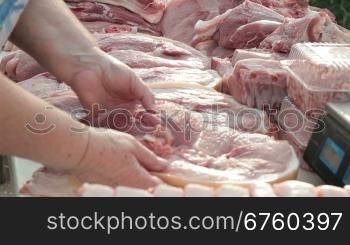 Selling pork at street market, female customer choosing a piece of meat