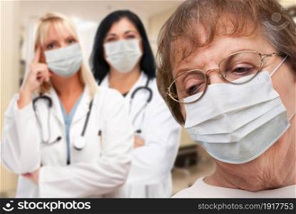 Senior Adult Female Looking Down as Doctors stand Behind All Wearing Medical Face Masks.