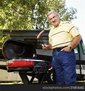 Senior adult man grilling hotdogs with RV in background.